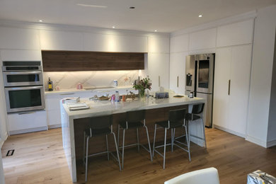 Inspiration for a mid-sized modern l-shaped laminate floor and brown floor kitchen remodel in Toronto with a double-bowl sink, white backsplash, ceramic backsplash, stainless steel appliances, an island and white countertops