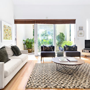 Inspiration for a transitional family room in Melbourne with white walls, light hardwood floors, a freestanding tv and beige floor.