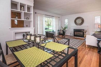 Example of a large trendy formal and open concept medium tone wood floor and brown floor living room design in Detroit with white walls, a standard fireplace, a brick fireplace and no tv