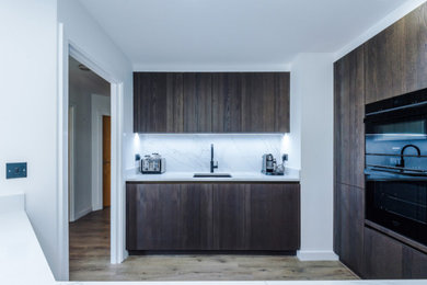 Design ideas for a small modern open plan kitchen in Manchester with a built-in sink, quartz worktops, engineered quartz splashback, black appliances, light hardwood flooring and a breakfast bar.