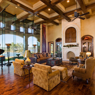 Imagen de salón para visitas abierto, mediterráneo, extra grande, con paredes beige, suelo de madera en tonos medios, chimenea tradicional, marco de chimenea de piedra, televisor retractable y suelo marrón