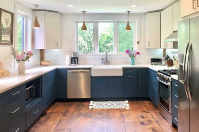 Photo of a large contemporary u-shaped eat-in kitchen in New York with a farmhouse sink, flat-panel cabinets, blue cabinets, quartz benchtops, white splashback, ceramic splashback, stainless steel appliances, medium hardwood floors, no island, brown floor and white benchtop.