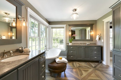 This is an example of a large country master bathroom in Minneapolis with louvered cabinets, grey cabinets, a freestanding tub, grey walls, medium hardwood floors, an undermount sink, granite benchtops, brown floor and brown benchtops.