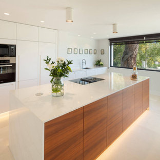 Modelo de cocina lineal, contemporánea, grande, abierta, con fregadero encastrado, armarios con paneles lisos, puertas de armario de madera clara, electrodomésticos negros, suelo de mármol, una isla y suelo beige