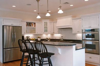 Inspiration for a large timeless l-shaped medium tone wood floor kitchen pantry remodel in Boston with a drop-in sink, raised-panel cabinets, white cabinets, limestone countertops, white backsplash, stainless steel appliances and an island