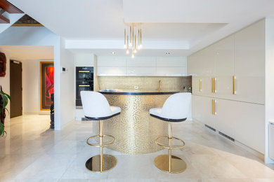 This is an example of a large modern l-shaped open plan kitchen in Sydney with a submerged sink, flat-panel cabinets, white cabinets, engineered stone countertops, metallic splashback, mosaic tiled splashback, black appliances, porcelain flooring, an island, beige floors, black worktops and a drop ceiling.