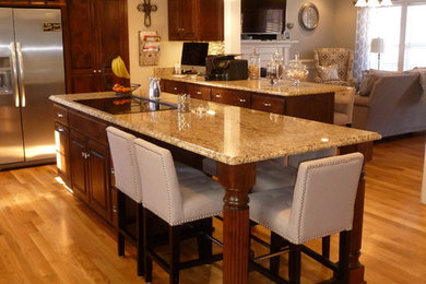 Large elegant l-shaped light wood floor eat-in kitchen photo in Nashville with a double-bowl sink, raised-panel cabinets, dark wood cabinets, granite countertops, green backsplash, glass tile backsplash, stainless steel appliances and two islands