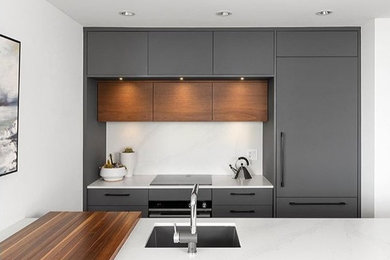Open concept kitchen - small modern galley laminate floor and gray floor open concept kitchen idea in Vancouver with an undermount sink, flat-panel cabinets, gray cabinets, quartz countertops, white backsplash, quartz backsplash, paneled appliances, a peninsula and white countertops