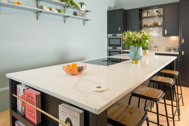 Photo of a large contemporary open plan kitchen in Other with a belfast sink, flat-panel cabinets, black cabinets, quartz worktops, stainless steel appliances, painted wood flooring, an island and white worktops.