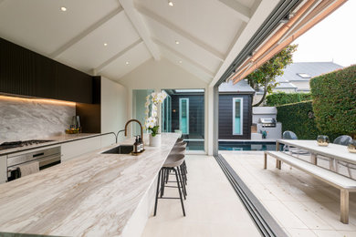 Medium sized contemporary galley kitchen/diner in Auckland with a built-in sink, white cabinets, marble worktops, white splashback, marble splashback, stainless steel appliances, ceramic flooring, an island, beige floors, white worktops and a vaulted ceiling.