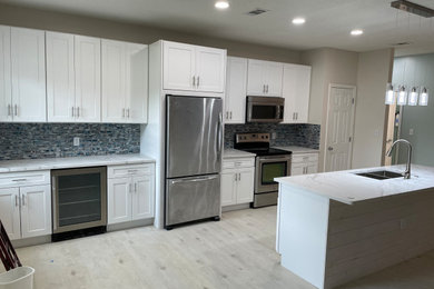 Inspiration for a single-wall vinyl floor and beige floor eat-in kitchen remodel in Other with an undermount sink, shaker cabinets, white cabinets, quartz countertops, blue backsplash, glass tile backsplash, stainless steel appliances, an island and white countertops
