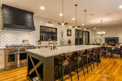 Large country l-shaped eat-in kitchen in Chicago with a farmhouse sink, flat-panel cabinets, white cabinets, quartzite benchtops, white splashback, subway tile splashback, stainless steel appliances, light hardwood floors, with island and brown floor.