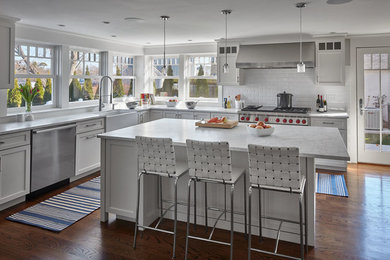 Photo of a mid-sized modern l-shaped kitchen in New York with a farmhouse sink, white cabinets, white splashback, subway tile splashback, stainless steel appliances, with island, medium hardwood floors, brown floor and shaker cabinets.