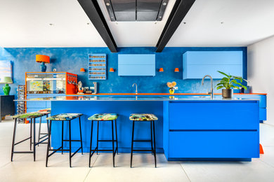 This is an example of a modern open plan kitchen in London with an integrated sink, flat-panel cabinets, blue cabinets, stainless steel worktops, black appliances, an island, grey worktops and a feature wall.
