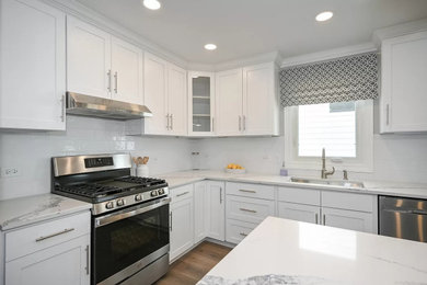 Mid-sized transitional l-shaped vinyl floor and brown floor eat-in kitchen photo in Chicago with an undermount sink, shaker cabinets, white cabinets, quartz countertops, white backsplash, subway tile backsplash, stainless steel appliances, an island and white countertops