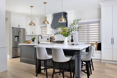 Photo of a mid-sized transitional l-shaped separate kitchen in Toronto with an undermount sink, shaker cabinets, white cabinets, quartz benchtops, white splashback, subway tile splashback, stainless steel appliances, medium hardwood floors, with island, white benchtop and beige floor.