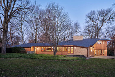 Large midcentury two-storey beige house exterior in New York with wood siding, a hip roof and a tile roof.