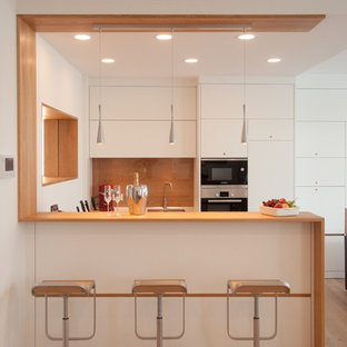 На фото: маленькие п-образные кухни-гостиные в современном стиле с врезной раковиной, плоскими фасадами, белыми фасадами, светлым паркетным полом, полуостровом и коричневым фартуком