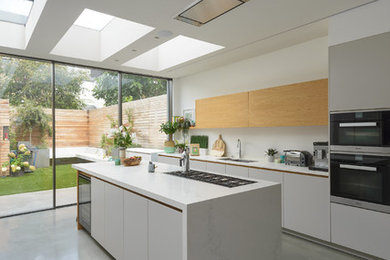 Open concept kitchen - mid-sized contemporary galley concrete floor and gray floor open concept kitchen idea in London with an integrated sink, flat-panel cabinets, gray cabinets, solid surface countertops, white backsplash, paneled appliances and an island