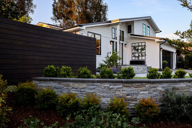 Idee per un giardino design esposto in pieno sole davanti casa con un muro di contenimento, pavimentazioni in cemento e recinzione in legno