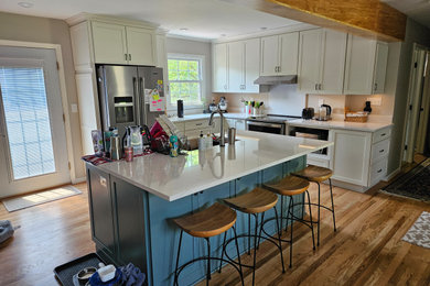 Example of a mid-sized transitional l-shaped medium tone wood floor and brown floor eat-in kitchen design in Louisville with a single-bowl sink, shaker cabinets, white cabinets, quartz countertops, white backsplash, quartz backsplash, stainless steel appliances, an island and white countertops