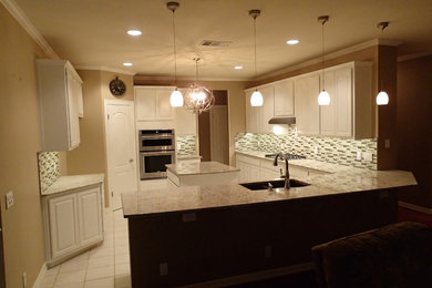 Inspiration for a large timeless galley kitchen pantry remodel in Austin with an undermount sink, recessed-panel cabinets, white cabinets, granite countertops, multicolored backsplash, stone tile backsplash, stainless steel appliances and an island