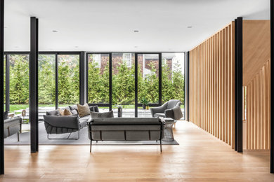 Huge trendy open concept light wood floor, brown floor and wood wall living room photo in New York