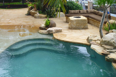 This is an example of a tropical backyard patio in Miami with a fire feature and natural stone pavers.