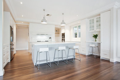Expansive traditional galley open plan kitchen in Sydney with an undermount sink, flat-panel cabinets, white cabinets, marble benchtops, white splashback, subway tile splashback, stainless steel appliances, light hardwood floors and multiple islands.