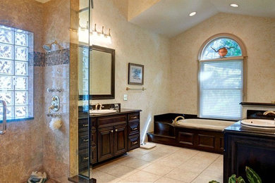 Design ideas for a large traditional master bathroom in Jacksonville with beaded inset cabinets, dark wood cabinets, a drop-in tub, an alcove shower, beige walls, a drop-in sink, granite benchtops, ceramic floors, beige floor and a hinged shower door.