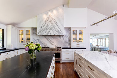 Example of a huge trendy u-shaped medium tone wood floor, brown floor and vaulted ceiling kitchen design in Salt Lake City with an undermount sink, flat-panel cabinets, white cabinets, marble countertops, white backsplash, marble backsplash, paneled appliances, two islands and black countertops