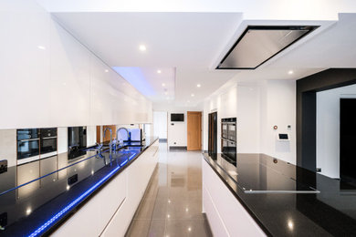 Large modern open plan kitchen in London with a double-bowl sink, flat-panel cabinets, white cabinets, granite worktops, mirror splashback, integrated appliances, porcelain flooring, an island, black floors and black worktops.