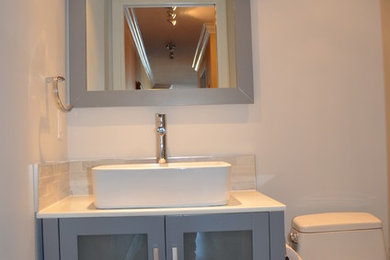 Small transitional 3/4 bathroom in Vancouver with a vessel sink, glass-front cabinets, grey cabinets, solid surface benchtops, a corner shower, a one-piece toilet, beige tile, mosaic tile, grey walls and pebble tile floors.