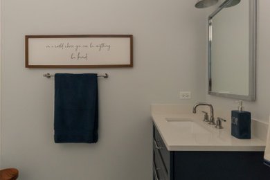 Diseño de cuarto de baño infantil, único y de pie campestre de tamaño medio con armarios estilo shaker, puertas de armario azules, bañera empotrada, combinación de ducha y bañera, sanitario de dos piezas, baldosas y/o azulejos blancos, baldosas y/o azulejos de cerámica, paredes blancas, suelo de baldosas de porcelana, lavabo bajoencimera, encimera de cuarzo compacto, suelo multicolor y encimeras blancas