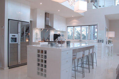 Design ideas for a modern u-shaped kitchen in Other with an undermount sink, flat-panel cabinets, white cabinets, solid surface benchtops, white splashback, glass sheet splashback, stainless steel appliances, concrete floors and with island.