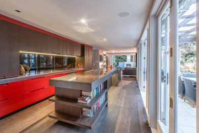 Design ideas for a mid-sized contemporary single-wall eat-in kitchen in Auckland with an undermount sink, flat-panel cabinets, orange cabinets, solid surface benchtops, black splashback, glass sheet splashback, black appliances, dark hardwood floors, with island, brown floor and brown benchtop.