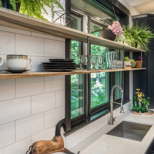 Пример оригинального дизайна: большая угловая кухня в стиле лофт с кладовкой, врезной раковиной, плоскими фасадами, черными фасадами, столешницей из кварцевого композита, белым фартуком, фартуком из керамогранитной плитки, техникой из нержавеющей стали, полом из цементной плитки, островом, серым полом и белой столешницей