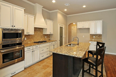 Open concept kitchen - mid-sized transitional galley ceramic tile open concept kitchen idea in Other with a double-bowl sink, raised-panel cabinets, white cabinets, granite countertops, beige backsplash, stone tile backsplash, stainless steel appliances and an island