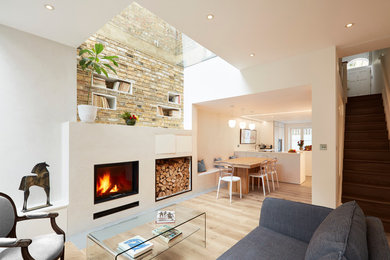 This is an example of a small contemporary open plan living room in London with white walls, light hardwood flooring, a plastered fireplace surround, no tv and a standard fireplace.