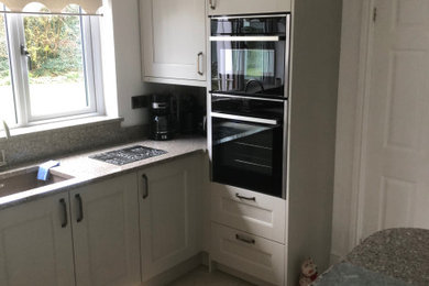 This is an example of a small classic l-shaped kitchen/diner in Cardiff with a submerged sink, shaker cabinets, beige cabinets, quartz worktops, brown splashback, glass sheet splashback, black appliances, porcelain flooring, a breakfast bar, beige floors, multicoloured worktops and feature lighting.