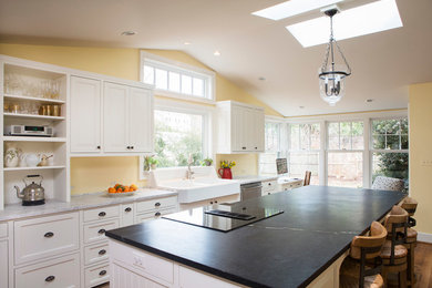 Mid-sized elegant single-wall medium tone wood floor eat-in kitchen photo in Other with a farmhouse sink, white cabinets, marble countertops, stainless steel appliances and an island