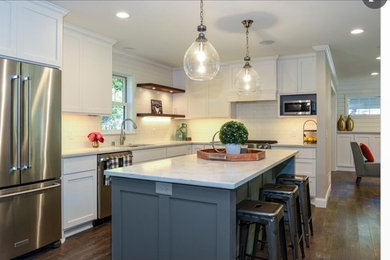 This is an example of a mid-sized transitional l-shaped eat-in kitchen in Minneapolis with white cabinets, white splashback, stainless steel appliances, medium hardwood floors, with island, brown floor, a drop-in sink, shaker cabinets, marble benchtops and subway tile splashback.