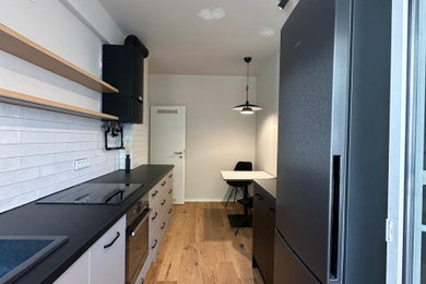Einzeilige, Kleine Moderne Schmale Küche mit Laminat-Arbeitsplatte, Küchenrückwand in Weiß, Rückwand aus Metrofliesen, braunem Holzboden und schwarzer Arbeitsplatte in Köln