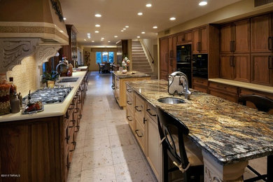Large tuscan galley ceramic tile enclosed kitchen photo in Phoenix with a double-bowl sink, recessed-panel cabinets, dark wood cabinets, granite countertops, beige backsplash, ceramic backsplash, black appliances and two islands