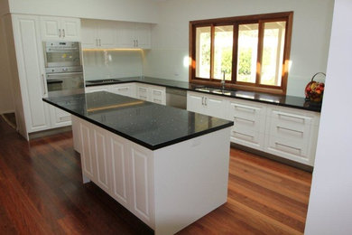 Inspiration for a mid-sized modern l-shaped kitchen in Sunshine Coast with an undermount sink, white cabinets, quartz benchtops, white splashback, stainless steel appliances, dark hardwood floors and with island.