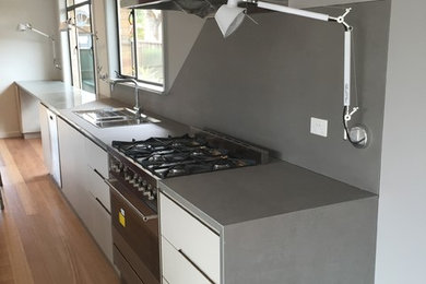 Photo of a modern kitchen in Melbourne with a drop-in sink, flat-panel cabinets, white cabinets, quartz benchtops, grey splashback, stainless steel appliances, medium hardwood floors and with island.