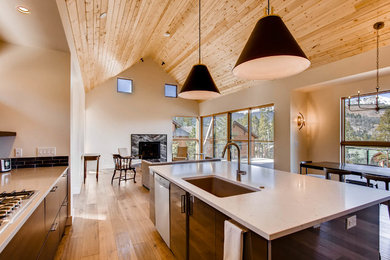Example of a large minimalist l-shaped medium tone wood floor and brown floor open concept kitchen design in Denver with an undermount sink, flat-panel cabinets, dark wood cabinets, solid surface countertops, black backsplash, glass tile backsplash, stainless steel appliances and an island