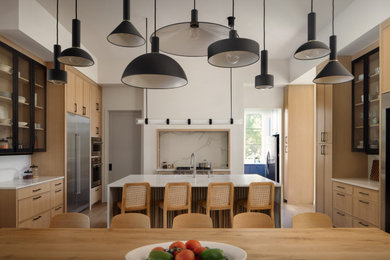 Trendy u-shaped light wood floor and beige floor kitchen photo in Austin with flat-panel cabinets, light wood cabinets, white backsplash, stone slab backsplash, stainless steel appliances, an island and white countertops