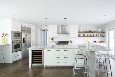 Large trendy l-shaped medium tone wood floor and brown floor eat-in kitchen photo in Kansas City with an undermount sink, flat-panel cabinets, white cabinets, marble countertops, white backsplash, ceramic backsplash, stainless steel appliances and an island