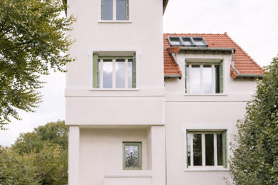 Exemple d'une façade de maison beige chic en pierre à trois étages et plus avec un toit en tuile et un toit rouge.